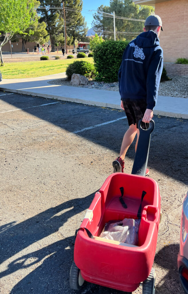 boy in a hoodie pulling a red plastic wagon