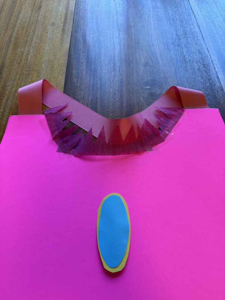 Back of a pink poster board Princess Peach costume showing ribbon straps secured with clear packing tape